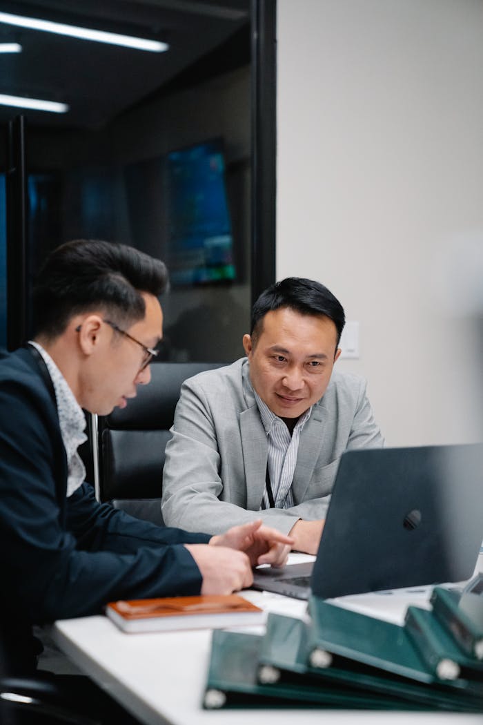 About Two men engaged in a business discussion over a laptop in a contemporary office.